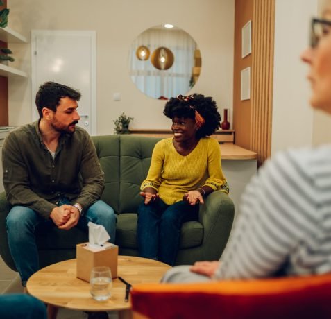 African american woman supporting new attender of group therapy to talk about himself during a meeting at mental health center. Group therapy participants sitting in a circle and talking.