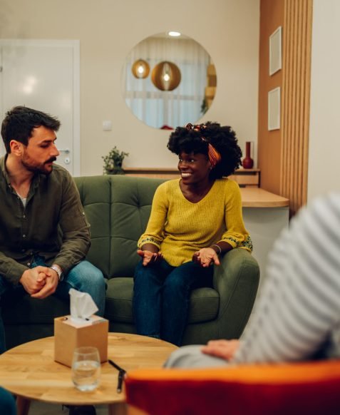 African american woman supporting new attender of group therapy to talk about himself during a meeting at mental health center. Group therapy participants sitting in a circle and talking.